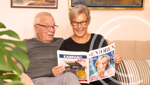 Äldre par som läser tidning hemma i soffan